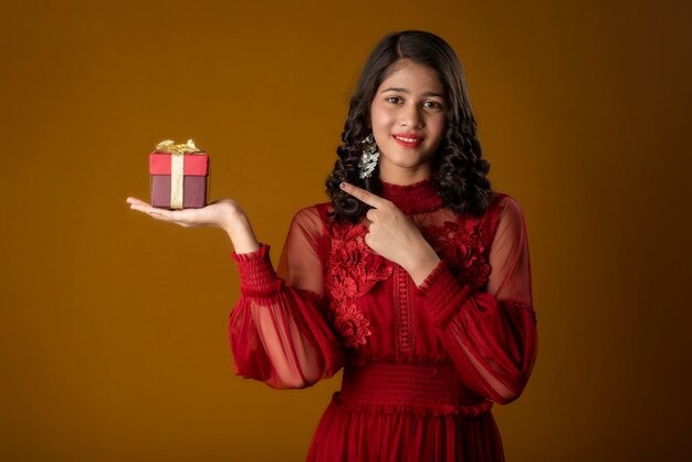 Retrato de joven sonriente feliz sosteniendo y posando con caja de regalo sobre fondo marrón