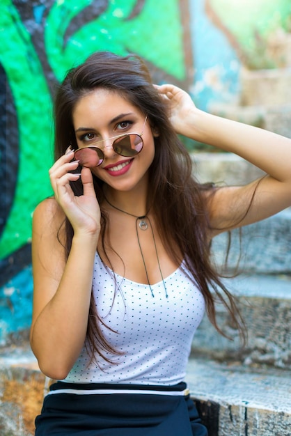 Foto retrato de una joven sonriente con gafas de sol en los escalones