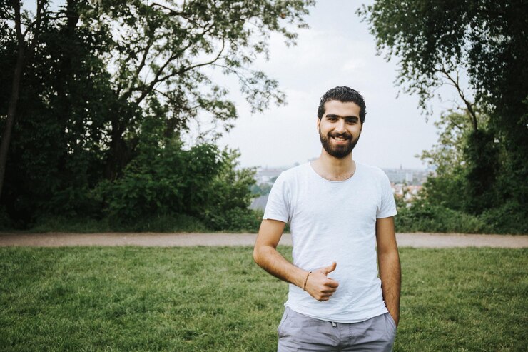 Foto retrato de un joven sonriente gestando los pulgares hacia arriba mientras está de pie en un campo de hierba