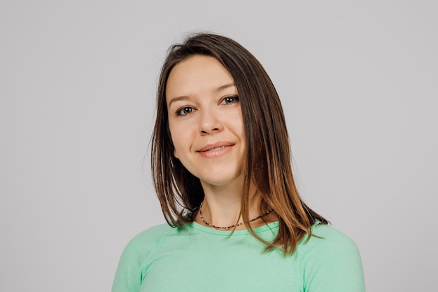 Retrato de una joven sonriente Hermosa morena feliz sonríe y posa sobre un fondo gris aislado que lleva una chaqueta verde