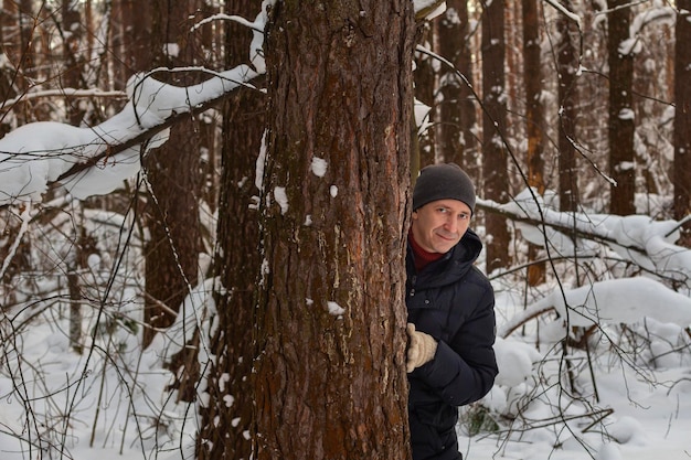 Retrato de un joven sonriente milenario que se asoma desde el tronco de un pino en un bosque de coníferas invernal