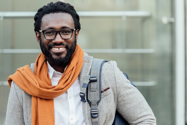Retrato de un joven sonriente con una mochila de pie en la ciudad
