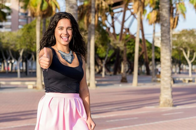 Foto retrato de una joven sonriente mostrando los pulgares hacia arriba mientras está de pie contra los árboles