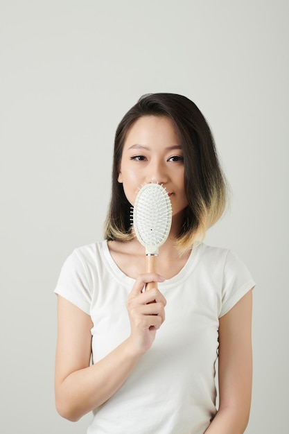 Retrato de una joven sonriente con un peinado fresco que muestra un cepillo de plástico que usa todos los días
