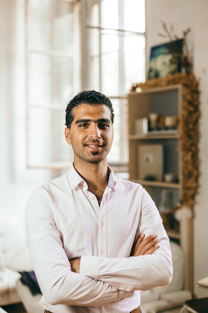 Retrato de un joven sonriente de pie con los brazos cruzados en casa