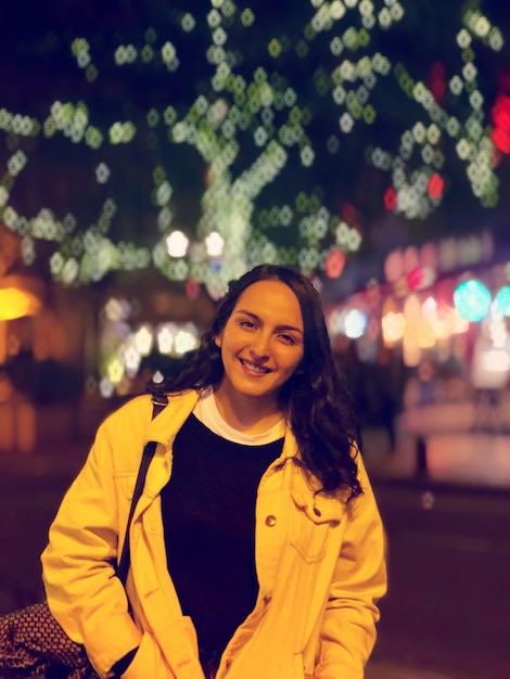 Foto retrato de una joven sonriente de pie en una ciudad iluminada por la noche