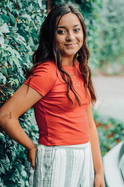 Foto retrato de una joven sonriente de pie junto a las plantas al aire libre