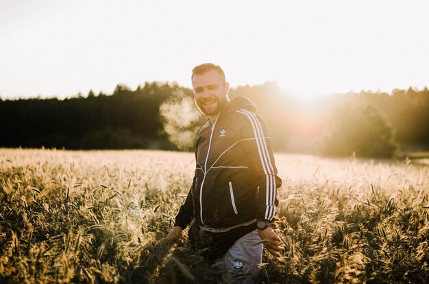 Retrato de un joven sonriente de pie en medio de plantas contra el cielo durante la puesta de sol