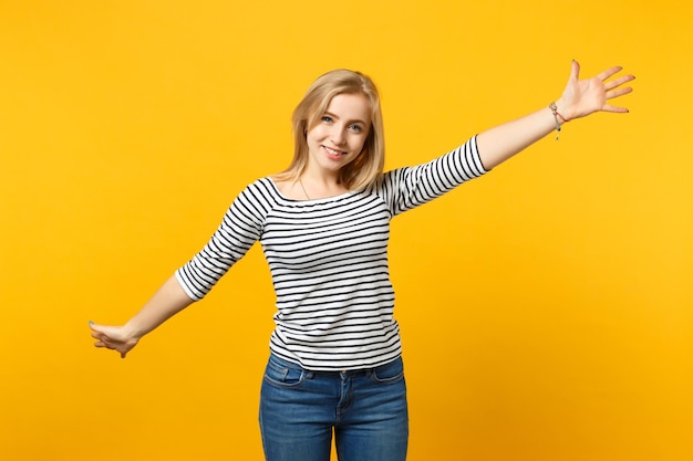 Retrato de una joven sonriente con ropa a rayas que mira la cámara, levantando las manos esparcidas aisladas en un fondo amarillo anaranjado en el estudio. Gente emociones sinceras concepto de estilo de vida. Simulacros de espacio de copia.