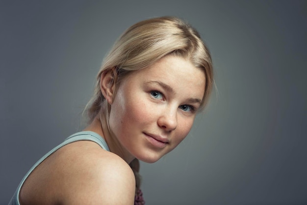 Retrato de una joven sonriente rubia linda con pecas y una trenza Pureza y juventud Closeup Fondo gris