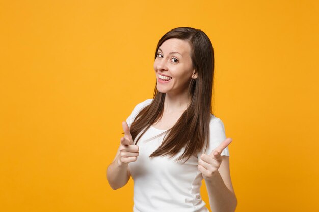 Retrato de una joven sonriente y segura de sí misma con ropa informal blanca que señala con el dedo índice a la cámara aislada en un fondo de pared naranja amarillo en el estudio. Concepto de estilo de vida de las personas. Simulacros de espacio de copia.