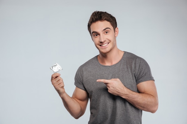 Retrato de un joven sonriente señalando con el dedo el condón en blanco