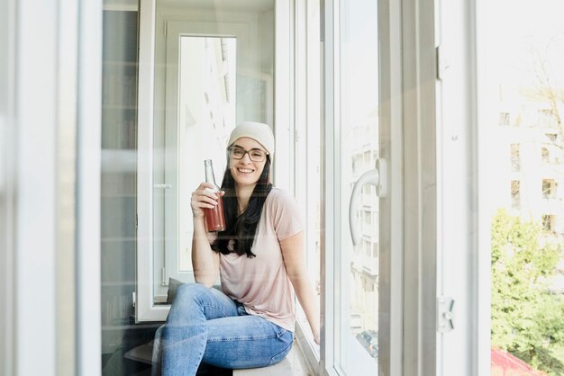 Retrato de una joven sonriente sosteniendo una botella en la ventana