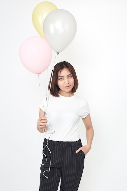 Foto retrato de una joven sonriente sosteniendo globos mientras está de pie contra un fondo blanco