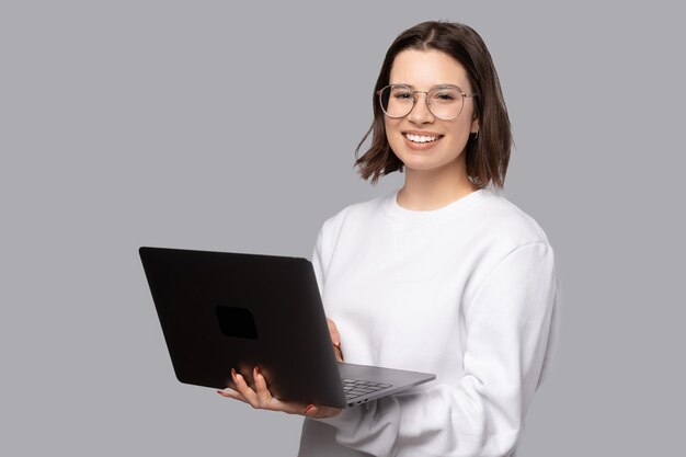 Retrato de una joven sonriente con suéter blanco sosteniendo una laptop y mirando a la cámara