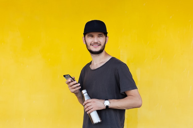 Retrato de joven sonriente con termo para agua y smartphone en manos