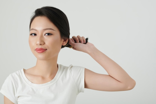 Retrato de una joven sonriente torciendo el cabello al hacer un bollo elegante