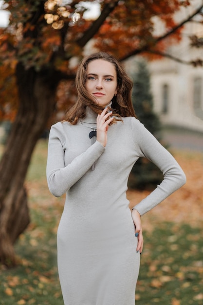 Retrato de joven sonriente con un vestido gris en el parque de otoño