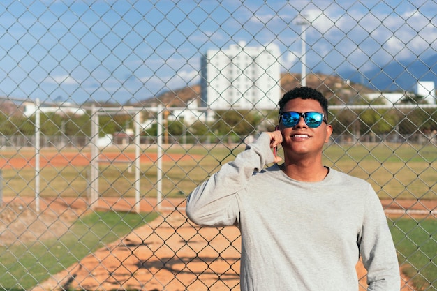 Retrato de un joven sonriente vistiendo una camiseta gris y gafas de sol.