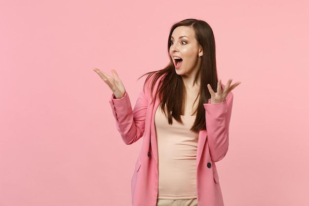 Retrato de una joven sorprendida con chaqueta mirando a un lado, manteniendo la boca abierta, esparciendo las manos aisladas en un fondo de pared rosa pastel. Emociones sinceras de la gente, concepto de estilo de vida. Simulacros de espacio de copia.