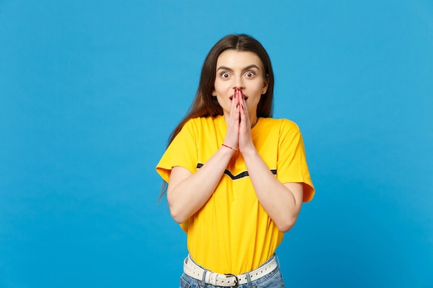 Retrato de una joven sorprendida sorprendida con ropa informal vívida que mira la cámara cubriendo la boca con las manos aisladas en un fondo azul brillante de la pared en el estudio. Concepto de estilo de vida de las personas. Simulacros de espacio de copia.