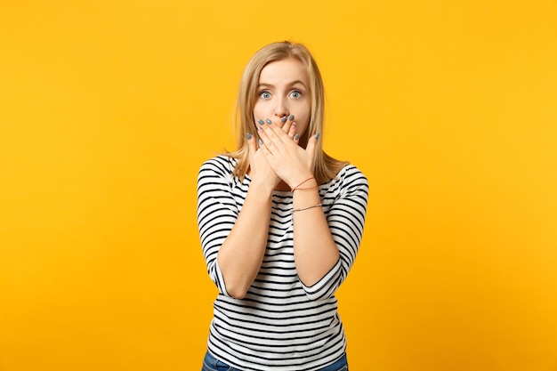 Retrato de una joven sorprendida sorprendida con ropa a rayas que cubre la boca con las manos aisladas en el fondo de la pared naranja amarilla en el estudio. Emociones sinceras de la gente, concepto de estilo de vida. Simulacros de espacio de copia.