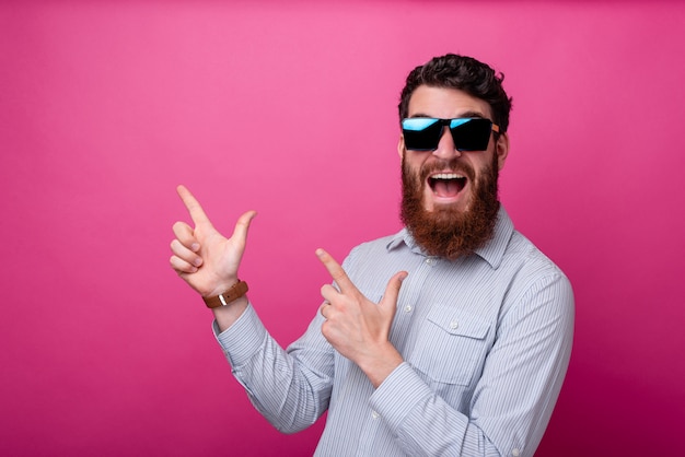 Retrato de joven sorprendido con barba apuntando lejos a copyspace