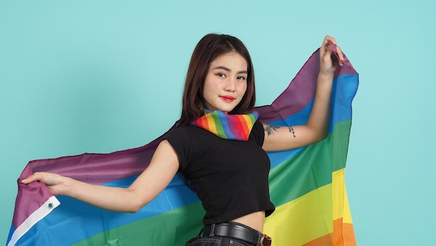 Retrato de una joven sosteniendo una bandera LGBT de pie contra un estudio de fondo verde azul