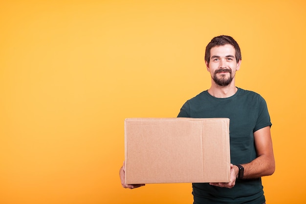 Foto retrato de un joven sosteniendo una caja mientras está de pie contra un fondo amarillo