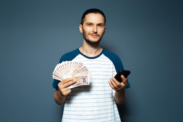 Retrato de joven sosteniendo dinero billetes de banco moldavos y teléfono inteligente en azul