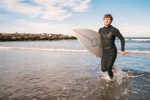 Retrato de joven surfista dejando el agua con tabla de surf bajo el brazo