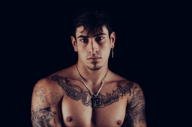 Retrato de un joven con tatuajes y joyas de plata con motivos violentos en un fondo negro