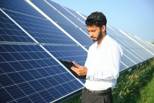 Retrato de joven técnico o gerente indio con ropas formales de pie con panel solar hombre de energía renovable de pie con el brazo cruzado espacio de copia