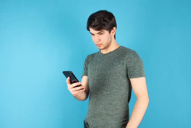 Retrato de un joven con un teléfono móvil contra el azul.