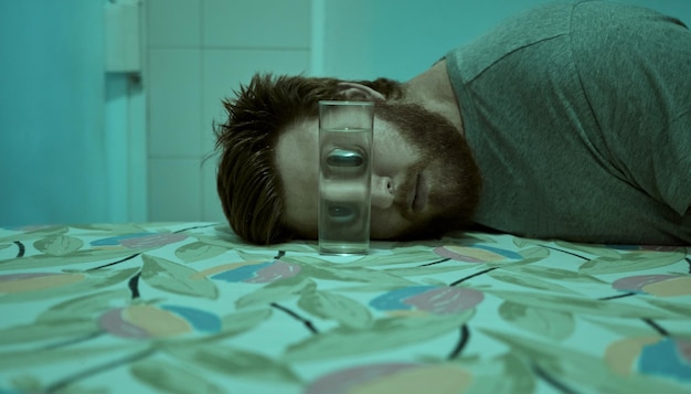 Retrato de un joven tendido junto al vaso de beber en la cama