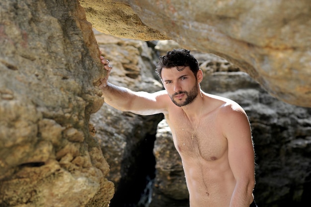 Retrato de joven en topless, al aire libre cerca de las rocas del mar, mirando a la cámara