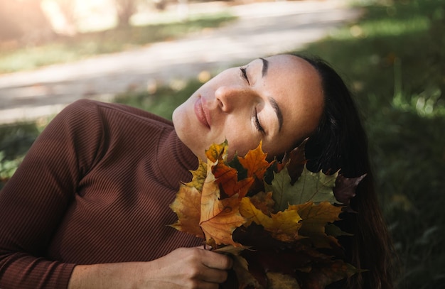 Retrato de una joven triste y hermosa tendida en el suelo de un bosque otoñal con hojas de arce coloridas Concepto lunes azul