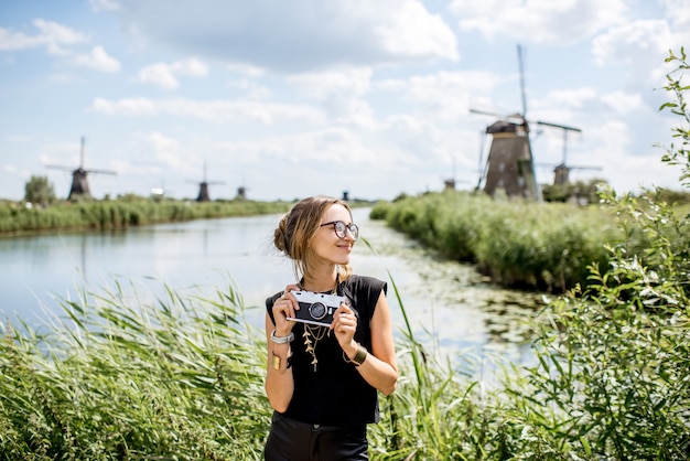 Retrato de una joven turista de pie con cámara de fotos en el fondo del hermoso paisaje con antiguos molinos de viento en Holanda