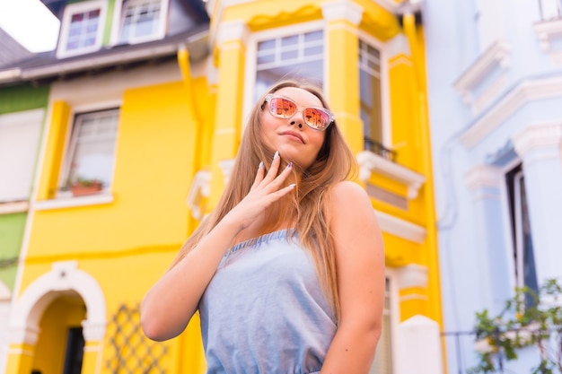 Retrato de una joven turista rubia con gafas de sol detrás de una colorida fachada amarilla y verde