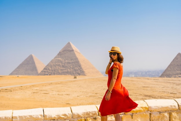 Foto retrato de un joven turista vestido de rojo disfrutando de las pirámides de giza