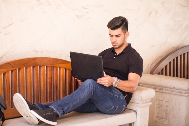 Retrato de un joven usando una computadora portátil en un banco