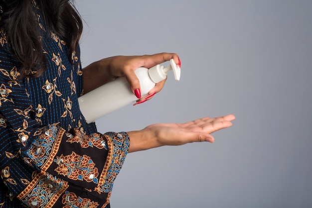 Retrato de joven usando o mostrando un gel desinfectante de una botella para limpieza de manos.