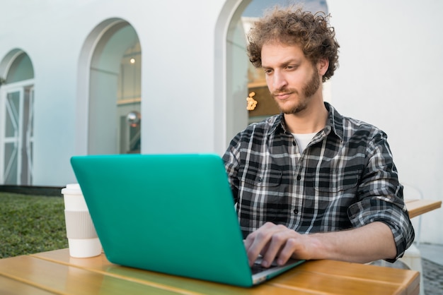 Retrato de joven usando su computadora portátil mientras está sentado en una cafetería