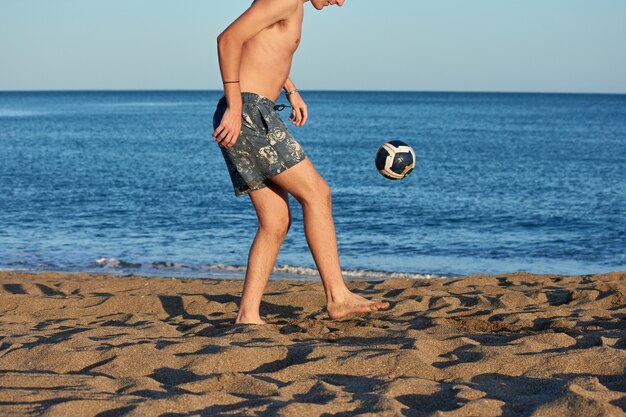 Un retrato de un joven varón caucásico en forma jugando con una pelota en la playa
