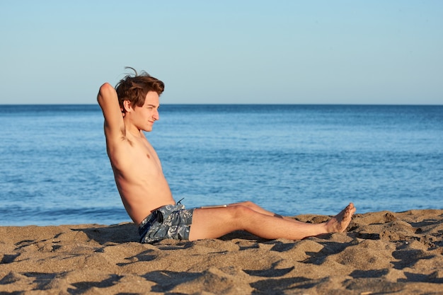 Un retrato de un joven varón caucásico en forma sentada en la playa