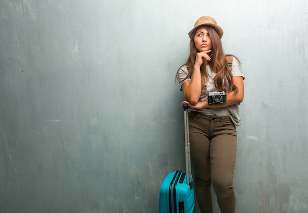 Retrato de joven viajero mujer latina contra una pared pensando y mirando hacia arriba