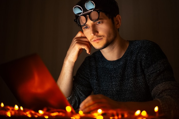 Retrato de joven vistiendo sombras, trabajando en el portátil en casa habitación oscura