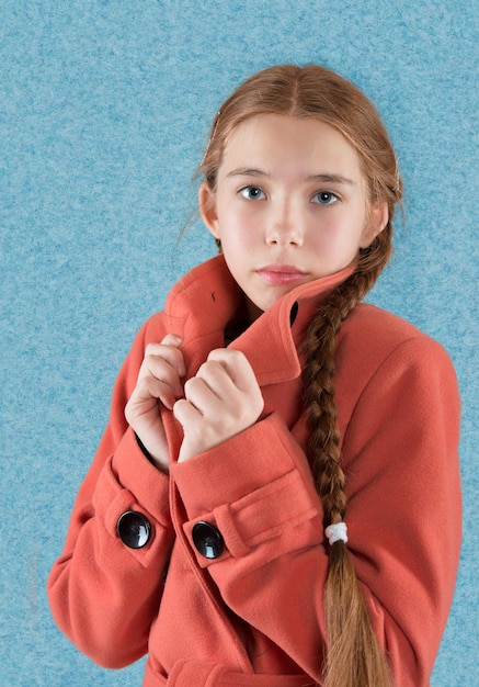 Retrato de una jovencita en abrigo rojo sobre fondo azul.