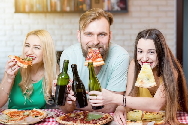 Retrato de jóvenes amigos divertidos vestidos casualmente con coloridas camisetas con rebanada de pizza y cerveza en casa