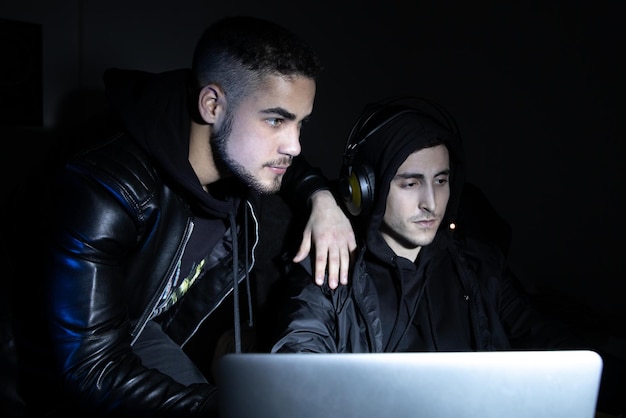 Retrato de jóvenes hackers en el trabajo. Hombres con ropa informal mirando la pantalla del portátil, escribiendo. Hackeo, concepto de computadora